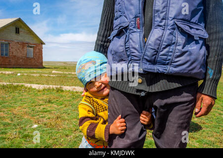 KEL-SUU, KYRGYZSTAN - AUGUST 13: Young Kyrgyz kid, aged around 2, hiding behind his dad. August 2016 Stock Photo