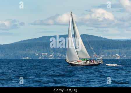 On a summer day, a middle-aged couple are at the helm of a Canadian yacht under sail in Malaspina Strait, near Powell River, British Columbia. Stock Photo