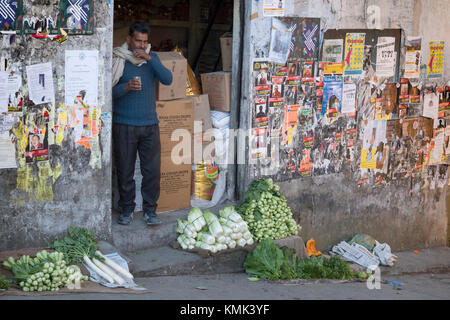 Man selling fresh vegetables drinks masala chai tea on shop doorstep Stock Photo