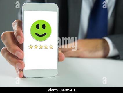 Digital composite of Hand holding phone with smiley face and 5 star feedback review rating Stock Photo