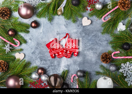 Christmas Frame made from Xmas Tree Branches, Baubles, Pine Cones, Candy Canes and Snowflakes on the Grey Background. Cute Little Winter Mittens in th Stock Photo