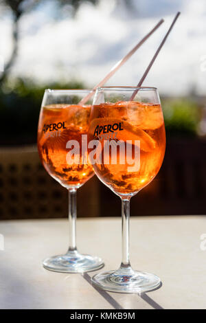 Two glasses of Aperol Spritz, a blend of Aperol, Prosecco and soda water with orange, on a table in an outside bar. Stock Photo