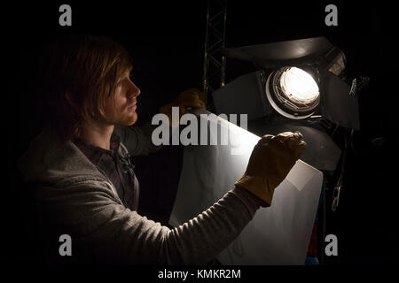 Lighting man placing a sheet of diffuser on a studio light in a Television studio Stock Photo