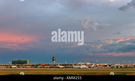 A magnificent cloudy evening sky over a modern airport, glowing with lanterns and windows, an airport building with a tower and a parked planes awaiti Stock Photo