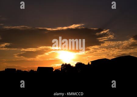 Sunset over the village, capturing the sun going behind the clouds Stock Photo