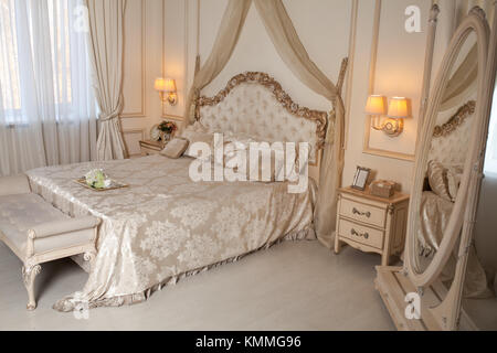 Big comfortable double bed in elegant classic bedroom in white and cream color Stock Photo