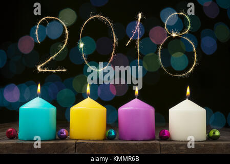 Multicolored burning candles with bokeh and digits 2018 on black background.Concept of New Year and Xmas Stock Photo