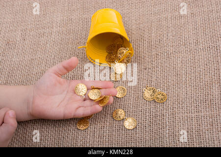 Bucket and fake gold coins in hand on canvas background Stock Photo