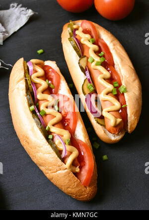 Tasty hot dogs with tomato, marinated cucumbers, onion on dark background Stock Photo