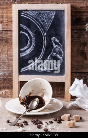 Cup of coffee ground with chalkboard on table with crumbs and crumpled napkin Stock Photo