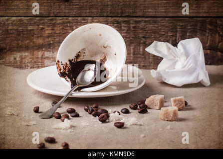 Cup of drunk coffee with coffee ground on table with crumbs, crumpled napkin and coffee beans over textured background Stock Photo