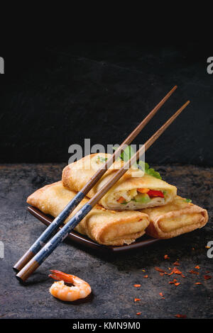 Fried spring rolls with vegetables and shrimps, served on squer ceramic plate with chopsticks over black background. Stock Photo