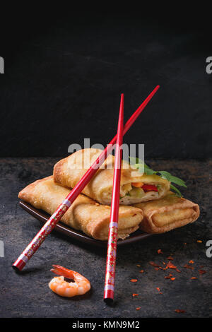 Fried spring rolls with vegetables and shrimps, served on squer ceramic plate with chopsticks over black background. Stock Photo