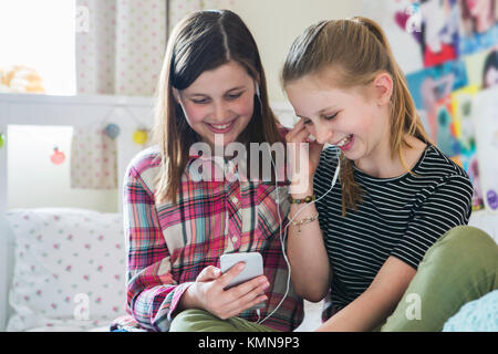 Two Girls Streaming Music From Mobile Phone In Bedroom Stock Photo