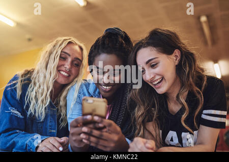 Laughing young female friends leaning on a laundromat counter using a cellphone together while doing laundry Stock Photo