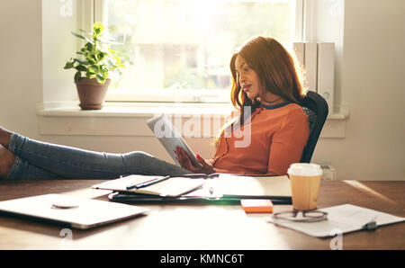 Young African female entrepreneur leaning back in a chair in her home office working online with a digital tablet Stock Photo
