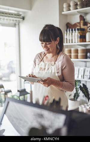Smiling young female florist checking her online orders using a digital tablet while working in her flower shop Stock Photo