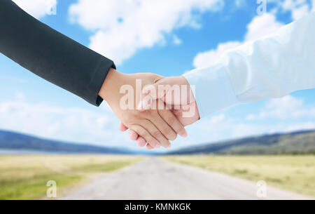 Hand of business man and woman hand shake metaphor cooperation and teamwork concept isolated on green field and blue sky background Stock Photo
