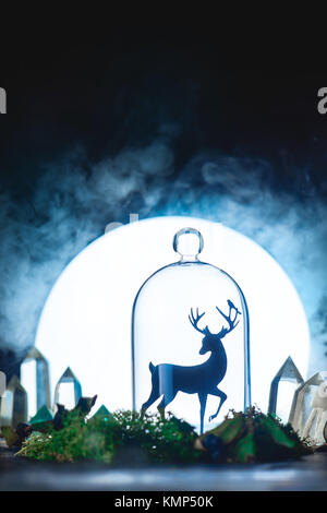 Magical forest with crystals and deer silhouette in a light of full Moon. Still life with glass dome and moss. Fairy tale concept with dark background and copy space. Stock Photo