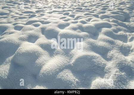 Fresh hilly snow surface background and drifting snowflakes. Bumpy snow covering winter landscape. Stock Photo