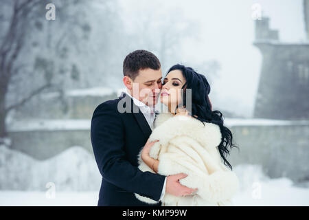 Close-up portrait of the beautiful newlywed couple tenderly hugging and touching cheeks during winter time. Stock Photo