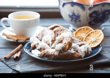 Bavarian cream puff with crushed hazelnut and lemon fondant on a blue plate. In the background, green tea with cinnamon sticks and a glass vase. Stock Photo