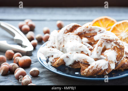 Bavarian cream puff with crushed hazelnut and lemon fondant on a blue plate. In the background a cup of tea and slices of dried oranges. Stock Photo