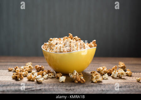 caramel popcorn in a yellow bowl on a wooden table background. popcorn in a bowl and scattered on table Stock Photo