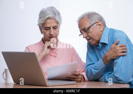 Senior couple looking at documents with laptop sitting on table Stock Photo