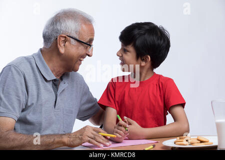 Grandfather and grandson coloring on paper with glass of milk and biscuits Stock Photo