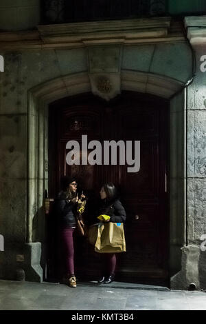 Two young women eating French fries (chips) in a doorway at night. Stock Photo