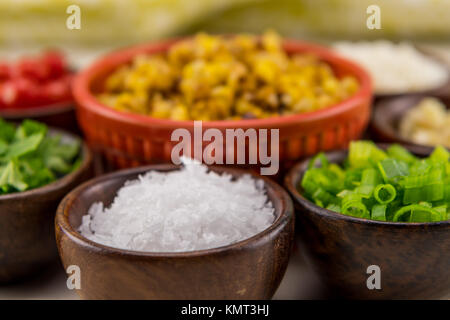 Flakes of Sea Salt in Wooden Bowl in front of roasted corn Stock Photo