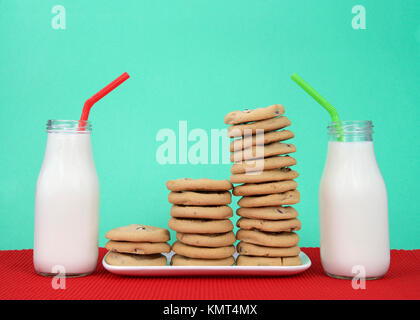 Chocolate chip cookies stacked at multiple heights on a white rectangular plate red placemat, green background. Two bottles of milk next to plate with Stock Photo