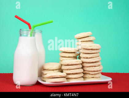 Sugar cookies stacked at multiple heights on a white rectangular plate red placemat, green background. Two bottles of milk next to plate with green an Stock Photo