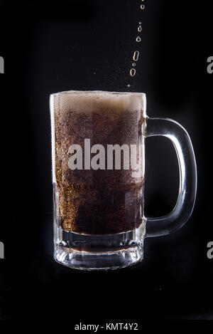 Cola being poured into a mug on an isolated black background. Stock Photo