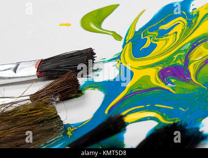 close up abstract background of paint brushes laying in colorful paint , blue,green, yellow,purple Stock Photo