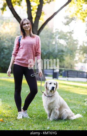 Portrait of brunette standing with labrador on lawn in summer park Stock Photo