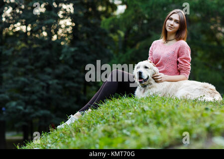 Photo from below of brunette sitting with dog on green lawn Stock Photo