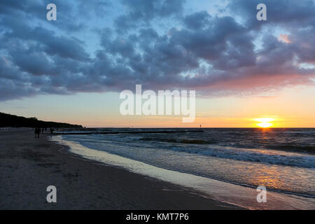 The sunset is seen from the beach of the Baltic Sea in Kolobrzeg. The waves of the sea lightly hits the sandy beach and there are some clouds in the s Stock Photo