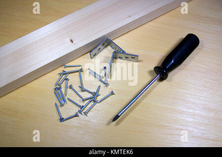 A wood with screws and brackets next to a screwdriver on a pine board Stock Photo