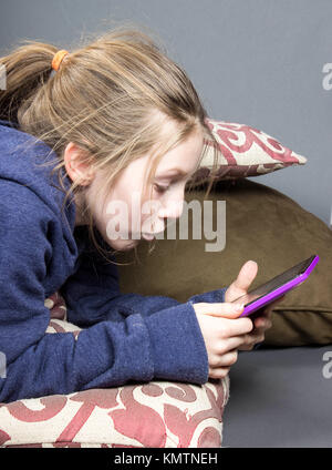 young child laying on stomach and pillows utilizing a hand held tablet, or the latest technology using wifi Stock Photo