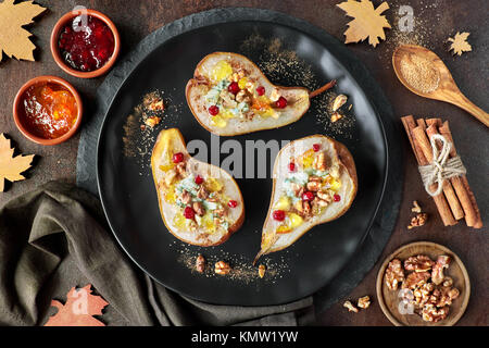 Pears baked with Blue cheese and wallnuts, served with orange and cowberry jam, cinnamon and sugar on dark background. Top view Stock Photo
