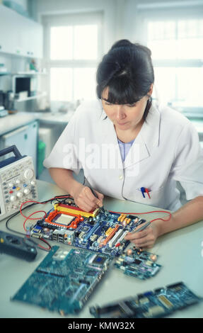 Young female tech or engineer repairs electronic equipment in research facility. Shallow DOF, focus on the eyelashes. This image is toned. Stock Photo
