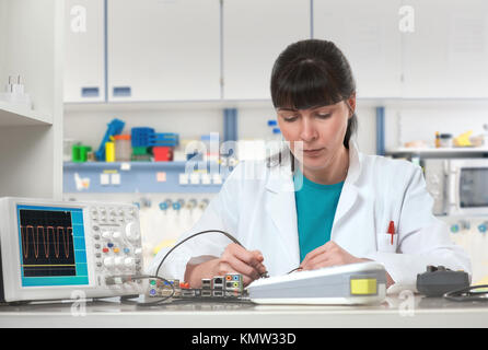 Young female tech or engineer repairs electronic equipment in research facility. Shallow DOF, focus on the eyelashes. This image is toned. Stock Photo