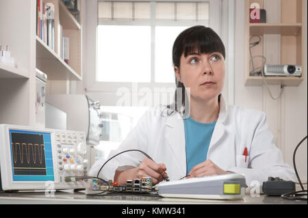 Young female tech or engineer repairs electronic equipment. Shallow DOF, focus on the face. Stock Photo