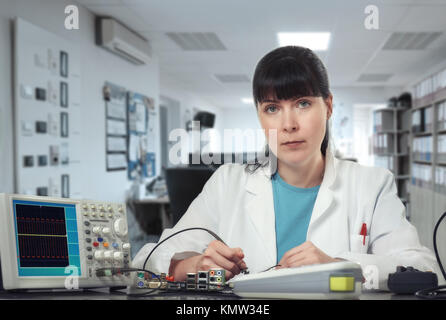 Young female tech or engineer repairs electronic equipment. Shallow DOF, focus on the face. Stock Photo