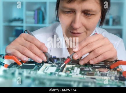 Middle-aged caucasian female engineer or tech repairs faulty motherboard in hardware repair shop. This image is toned. Stock Photo