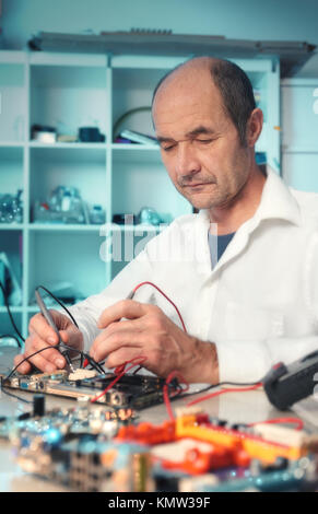 Senior male tech tests faulty motherboard in hardware service center, toned image Stock Photo
