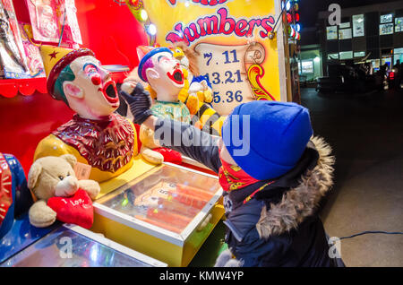 A boy plays a laughing clowns fairground game. It is a game of chance whereby you feed a 'clown' with balls which drop into a scoring rack. Stock Photo