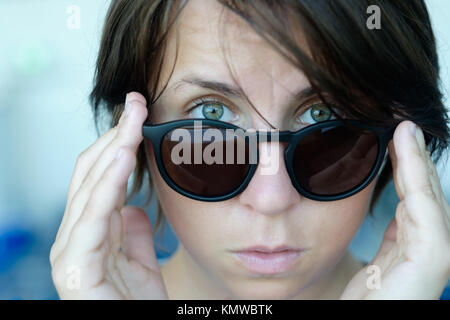 A disheveled girl without makeup takes off her black sunglasses in surprise. Hide your face and emotions concept . Stock Photo